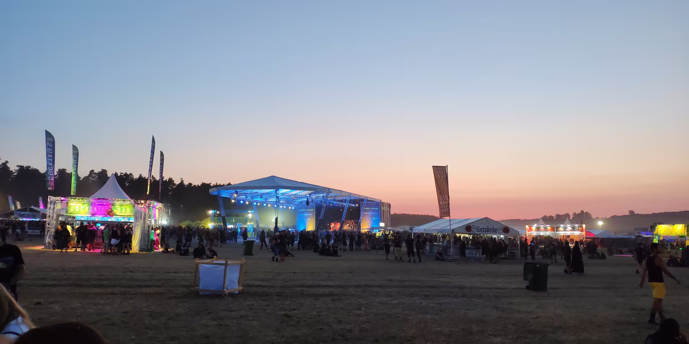 Festivalgelände am Abend mit beleuchteten Bühnen und Campingflächen